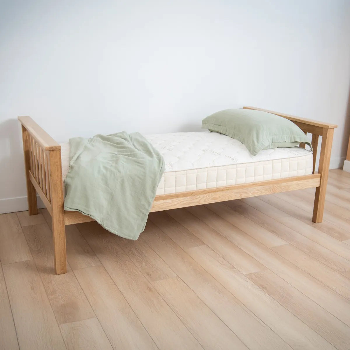 Wooden bed with green bedding on a wooden floor and white wall background